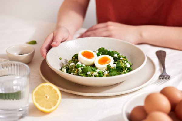 A boiled egg cut in half over a plate of smashed peas with a person waiting to eat