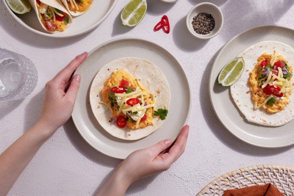 Two hands reaching for the plate of egg tacos